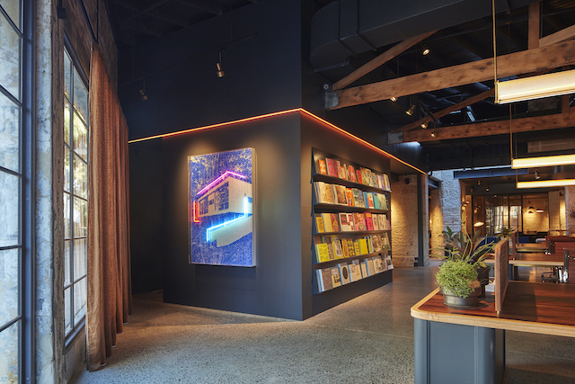 A neon artwork by Tom Adair hangs alongside an ever-changing array of books